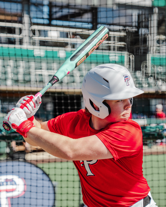 Baseball player in red uniform with white helmet swinging a bat in a batting cage.