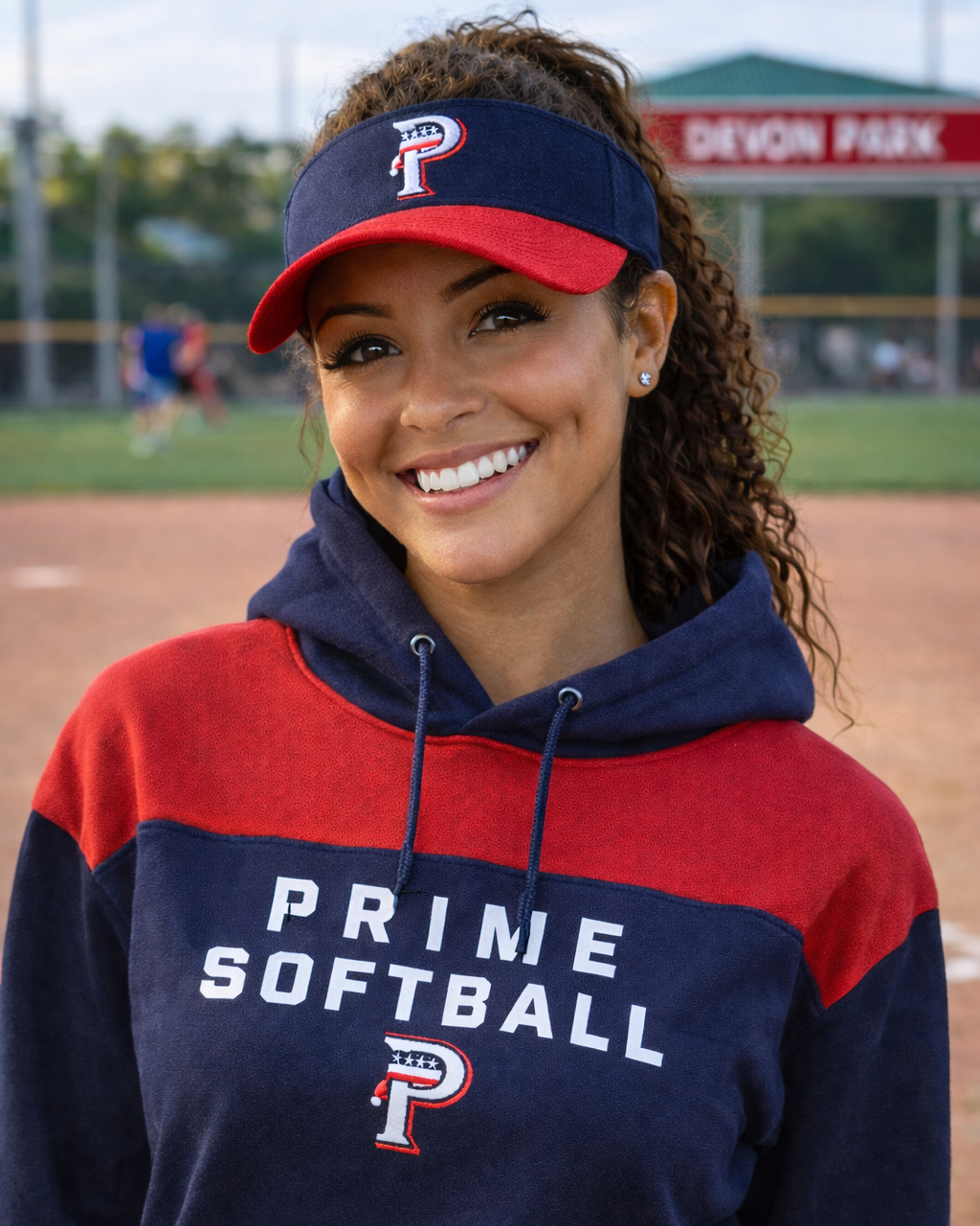 Person wearing a Prime Softball hoodie and visor on a sports field