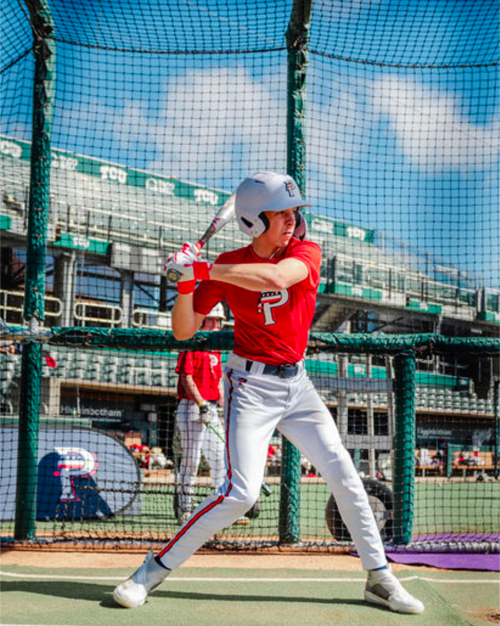 Baseball player in red jersey and white pants preparing to swing a bat on a field with a blue sky.