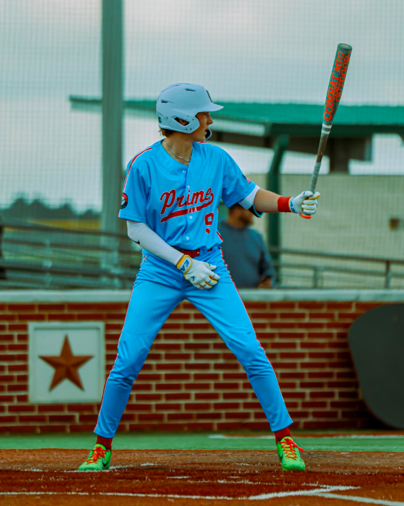 Baseball player in a blue uniform with 'Primos' on it, holding a bat on a baseball field.